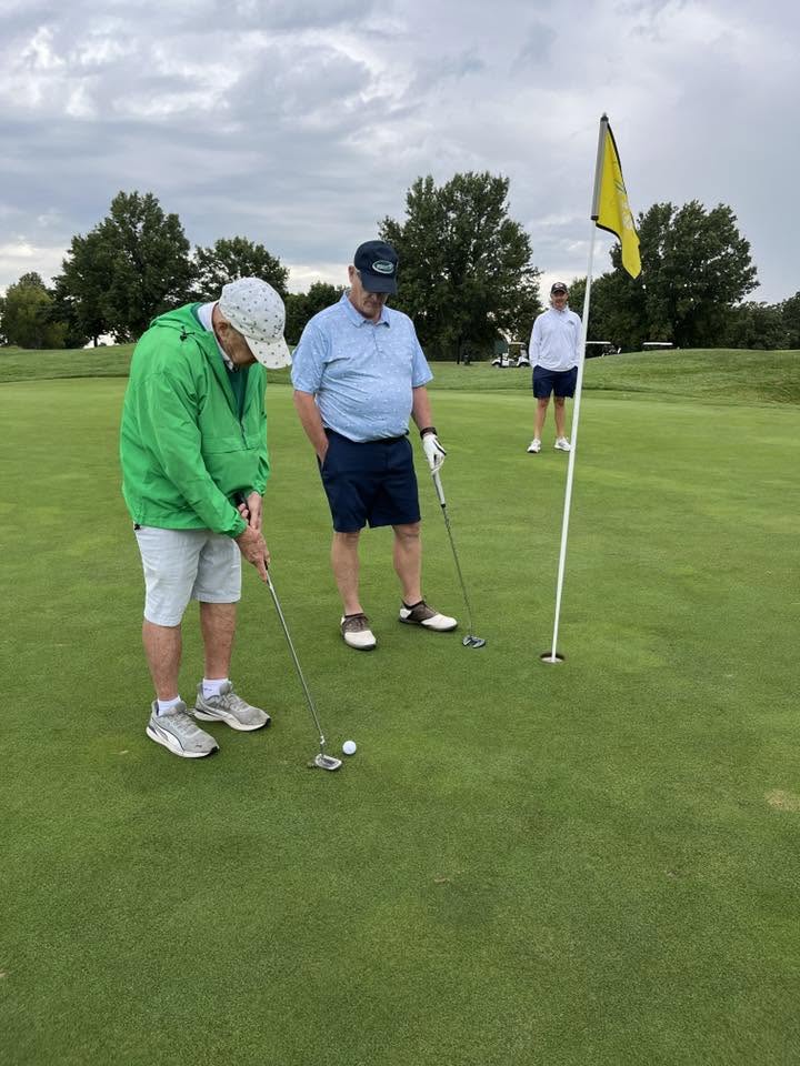 One man shooting a golf ball into the hole while another stands near